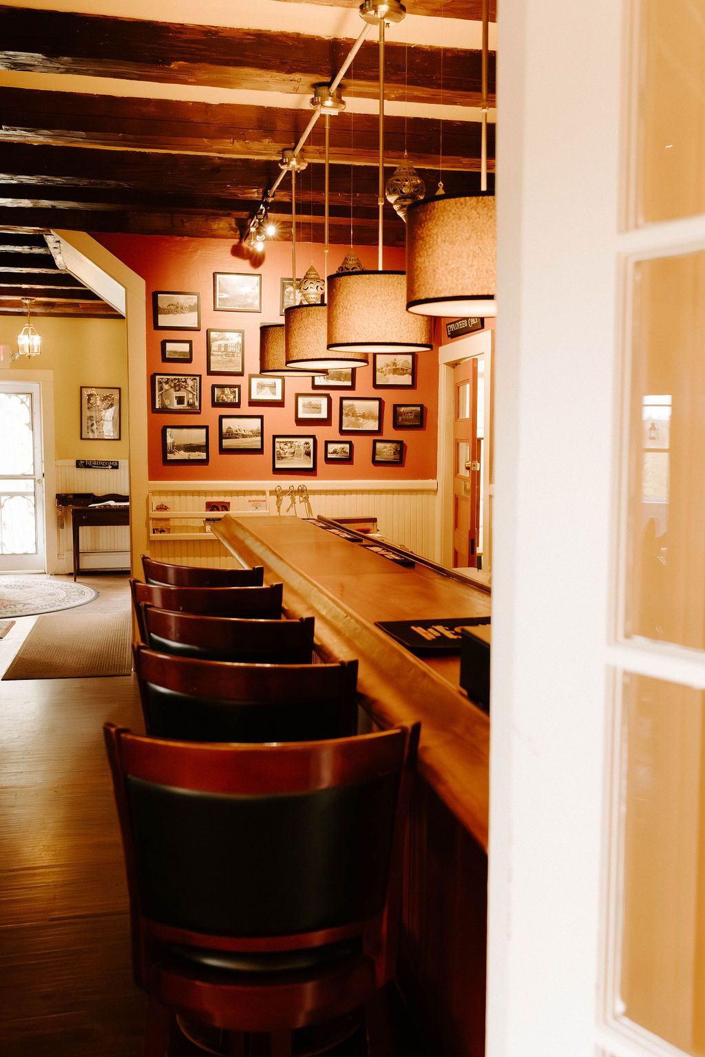 Cozy bar with wooden counter, high stools, hanging lights, and framed photos on the wall