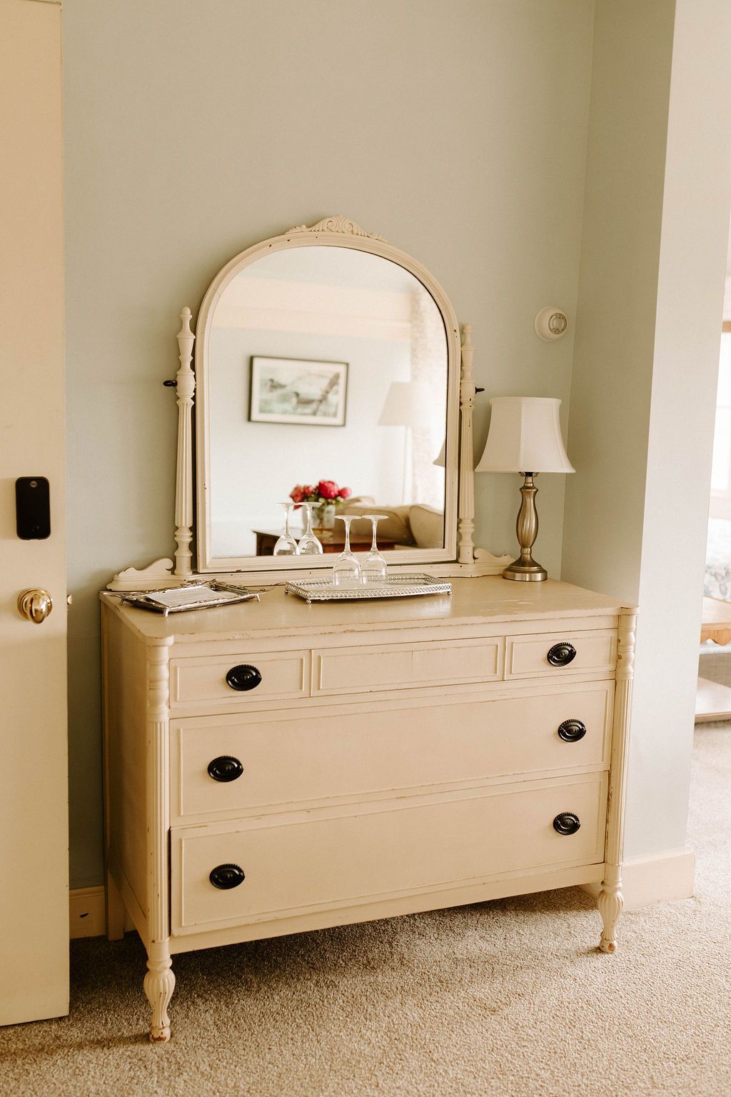 Cream dresser with oval mirror and lamp in a beige bedroom.