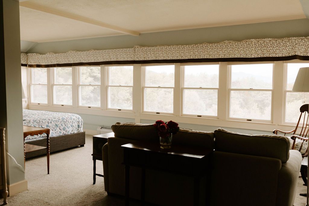 Bright living room with large windows, sofa, chair, and a bed by the wall