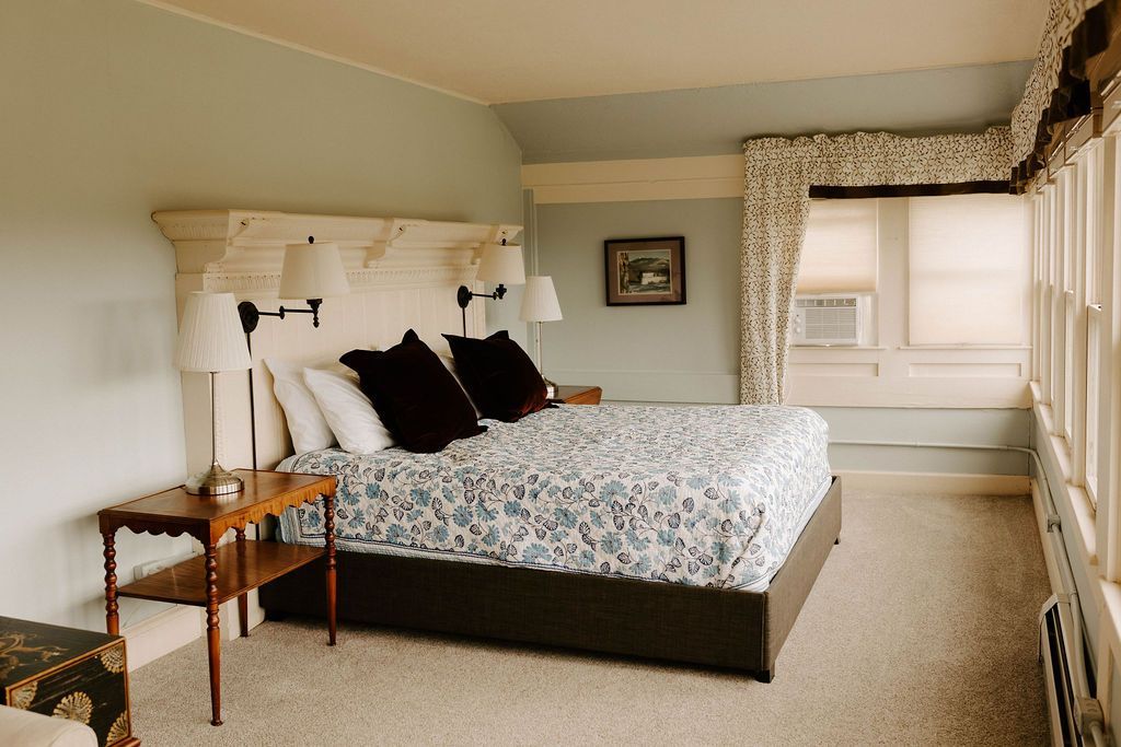 Bedroom with a large bed, tufted headboard, floral bedding, and a window seat by the bright window.