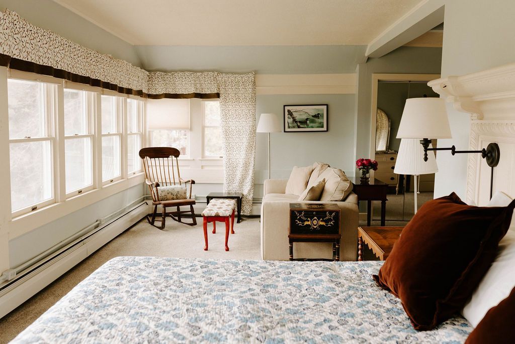 Bright bedroom with a bed, chair, sofa, large windows, and floral curtains