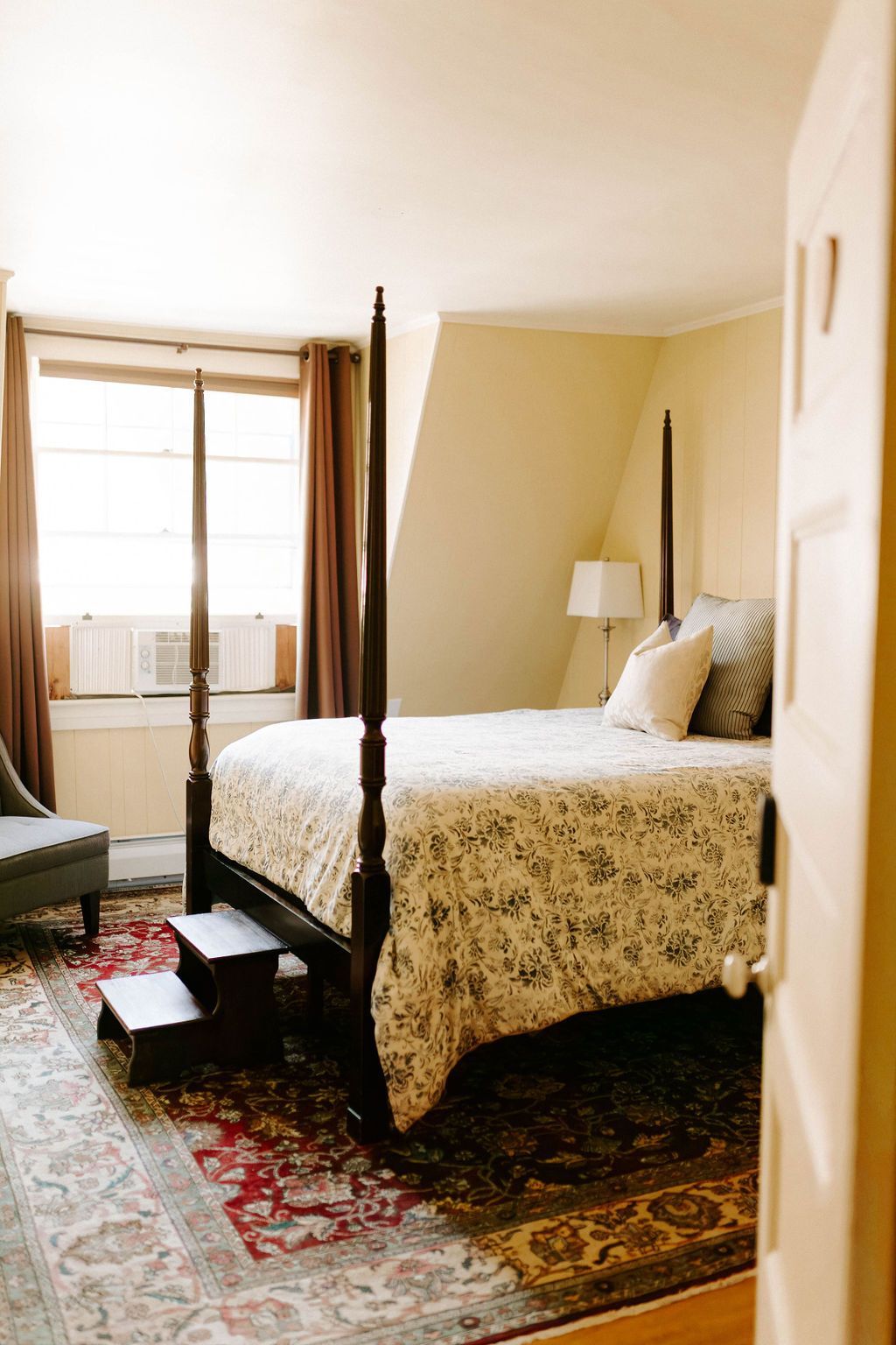 Cozy bedroom with a bed, patterned rug, window light, and a small lamp beside the headboard