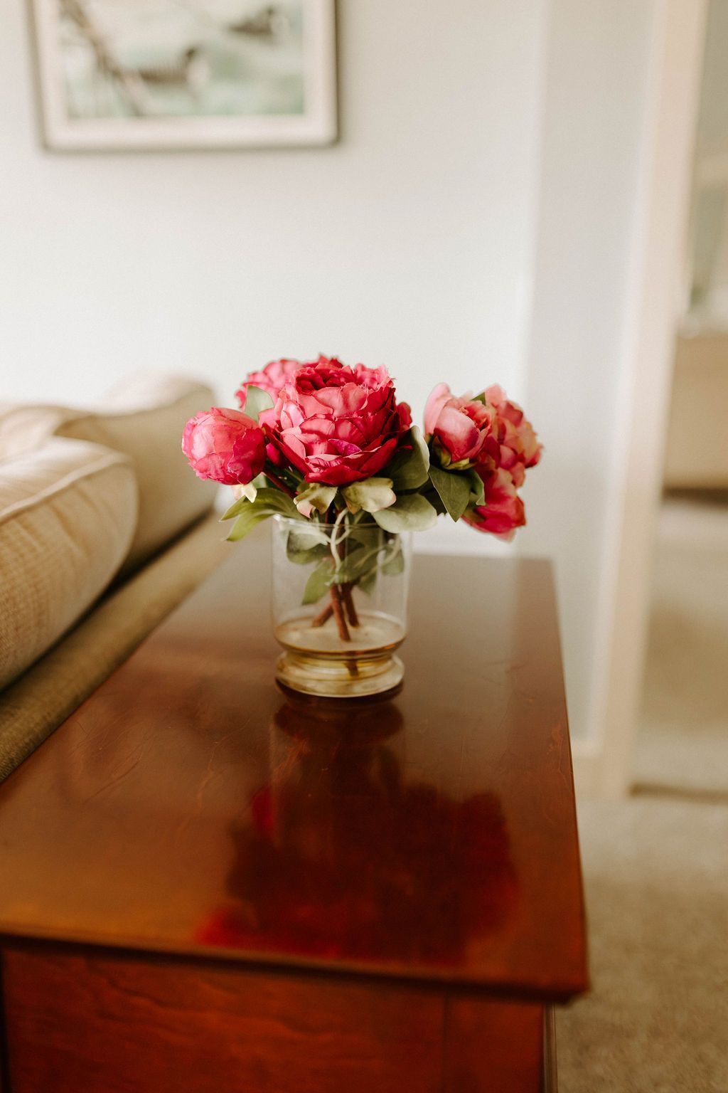 Small vase of pink flowers on a wooden table in a softly lit living room