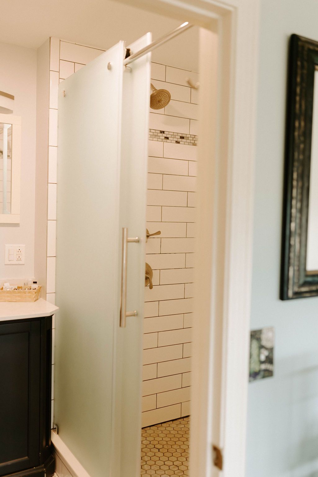 Open white door revealing a tiled shower area in a bright bathroom