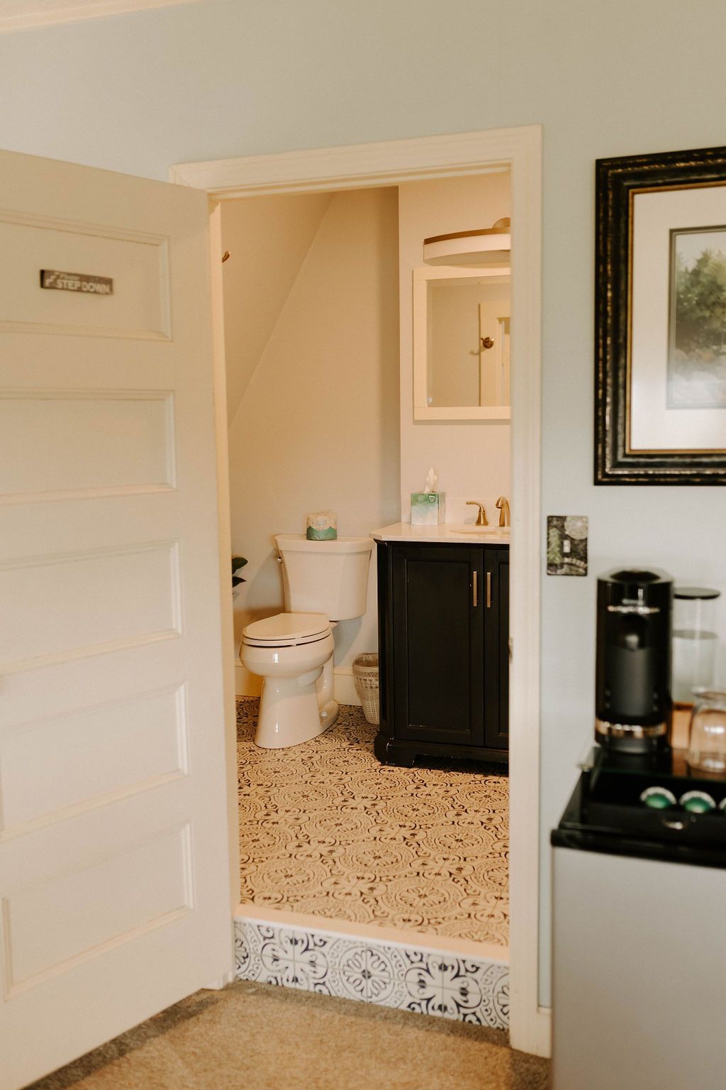 Bathroom doorway with white toilet, black vanity, and speckled tile floor visible from a hall