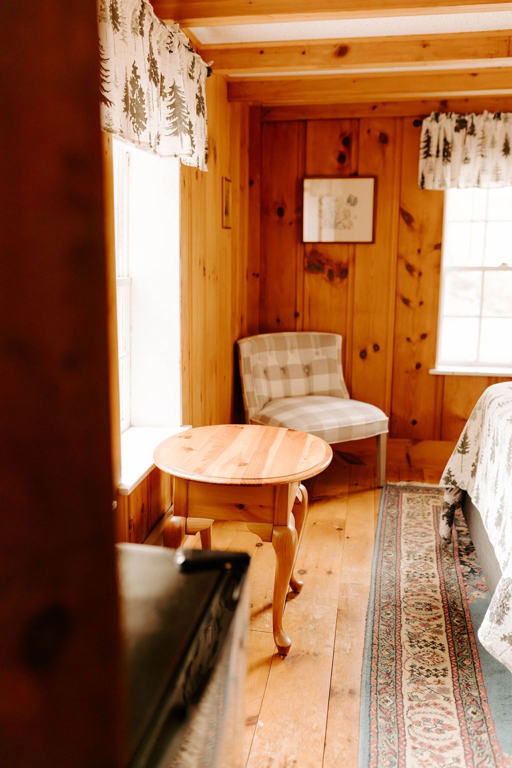 Cozy wood-paneled room with a small round table, upholstered chair, and sunlit window