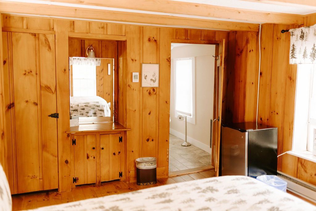 Wood-paneled bedroom with bed, dresser, mirror, and open doorway to a bright hall