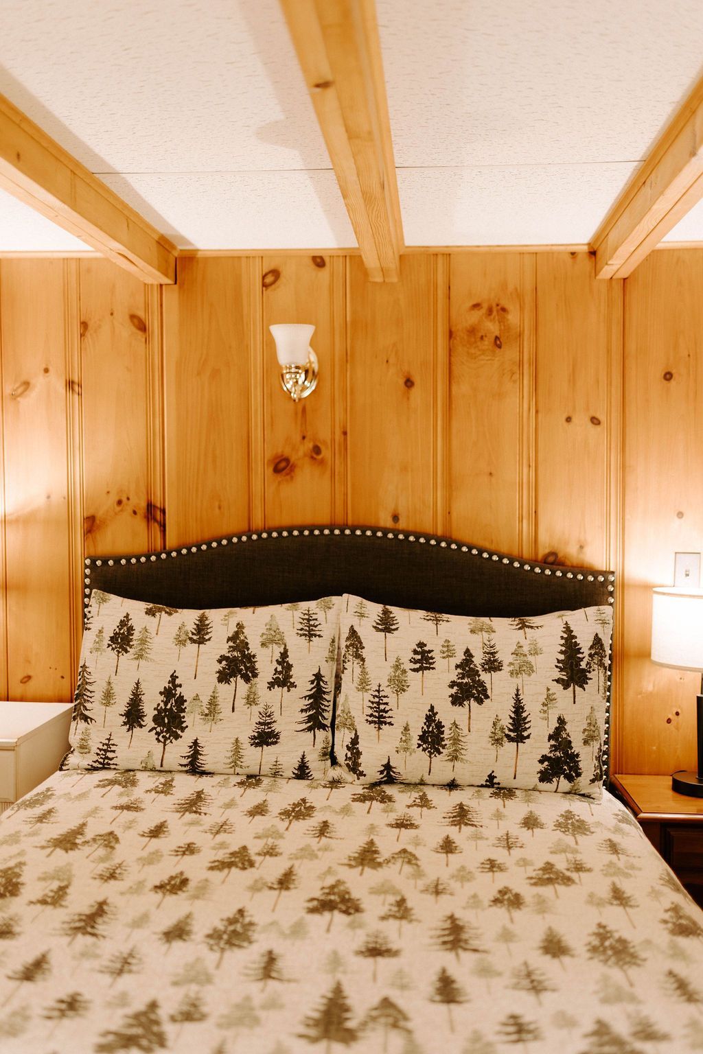 Cozy wooden cabin bedroom with a tree-patterned bedspread and headboard under exposed beams