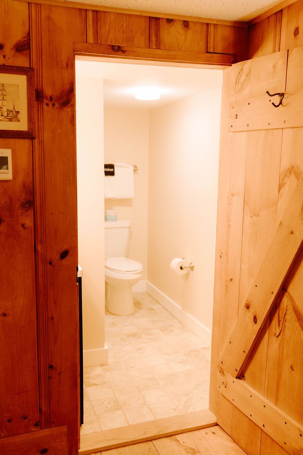 Open wooden door to a small beige bathroom with a toilet and shower visible.