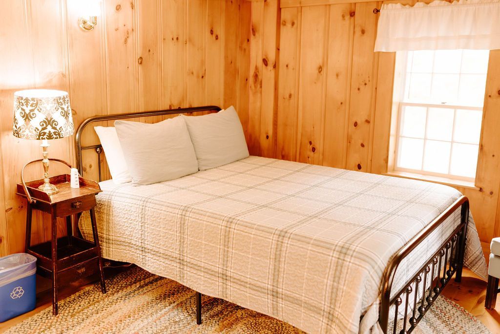 Cozy bedroom with wooden paneled walls, a bed, bedside lamp, and a window with white curtains