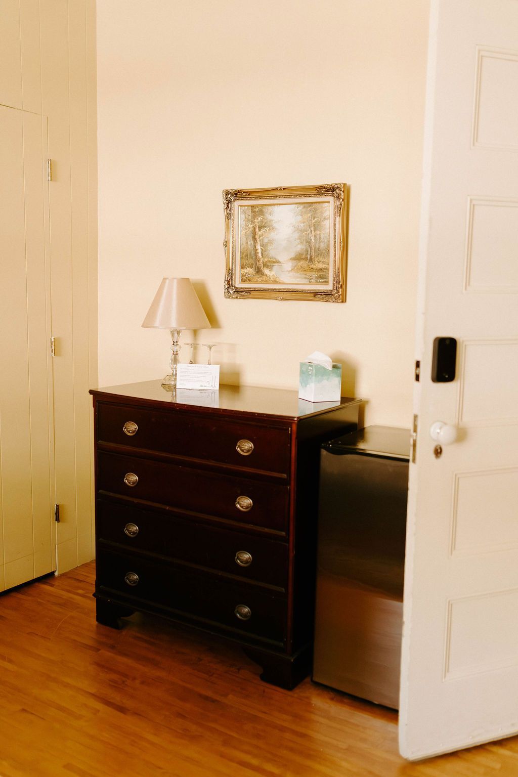 Dark wooden dresser with lamp and mirror beside an open door in a small room.