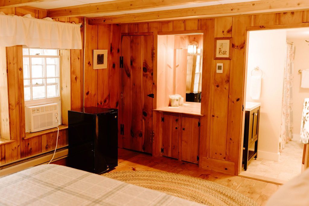 Wood-paneled bedroom with a bed, window, mirror, and open doorway to a bright adjoining room