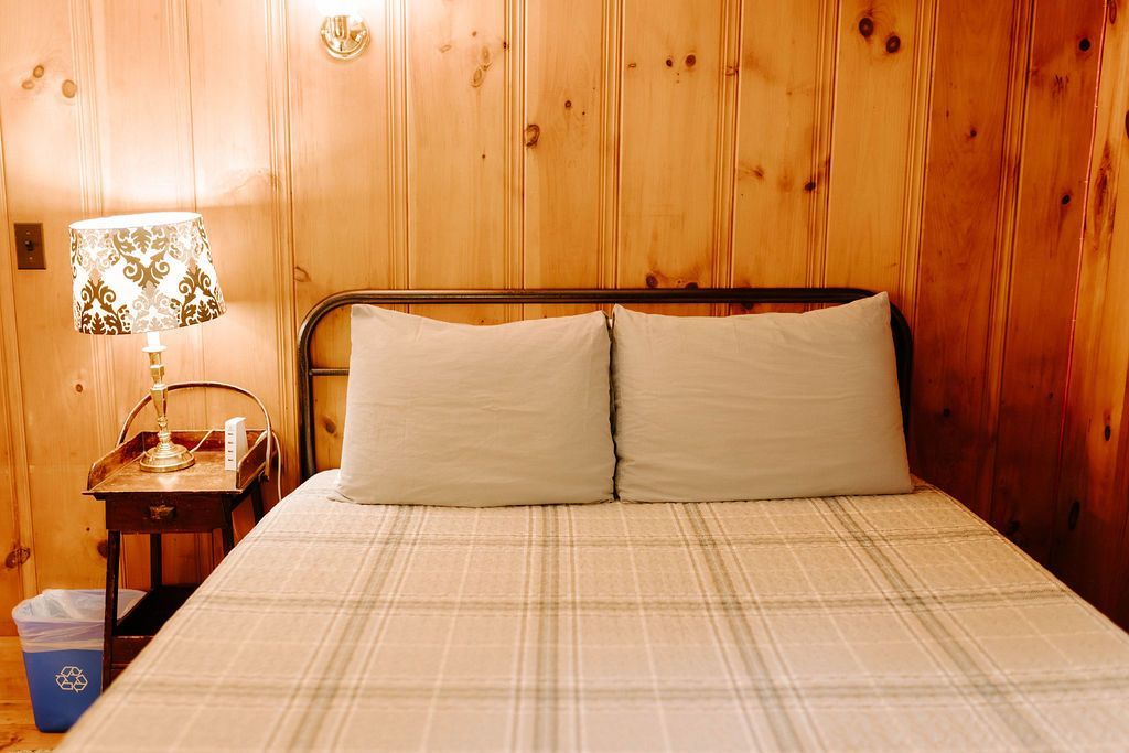 Cozy wood-paneled bedroom with a neatly made bed and a bedside lamp illuminated warmly.