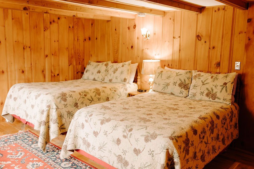 Two beds with floral bedding in a cozy wood-paneled bedroom