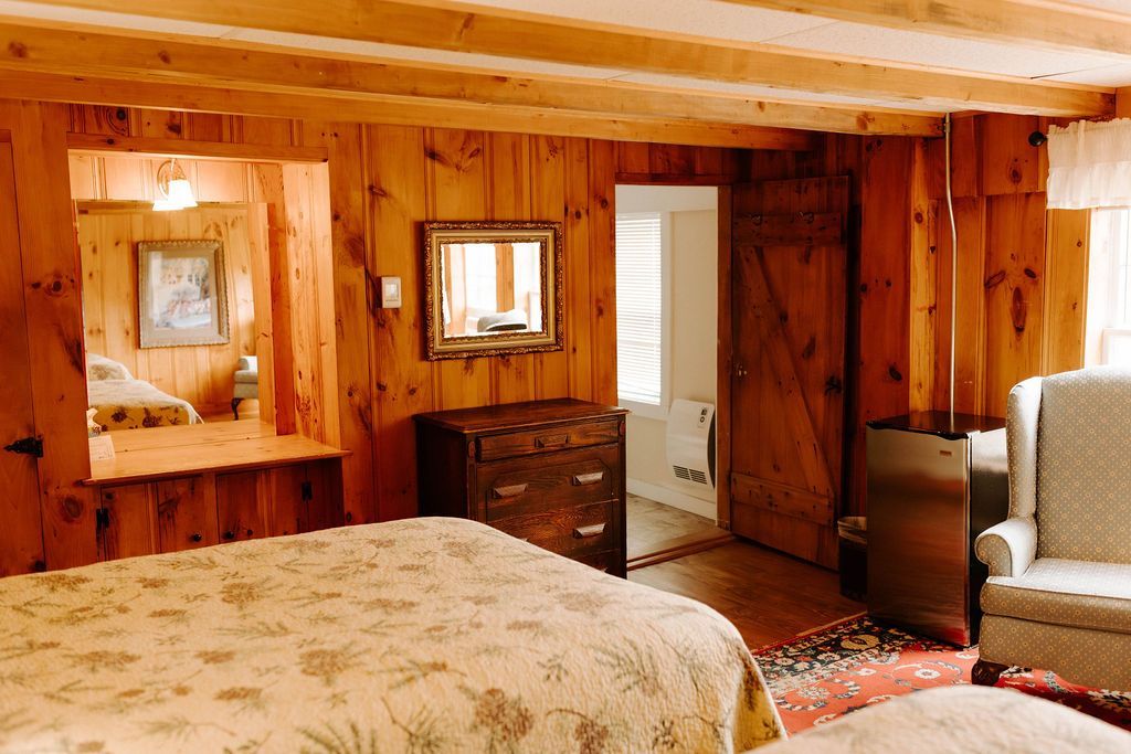 Cozy wood-paneled bedroom with bed, dresser, mirror, window, and open doorway to a bathroom