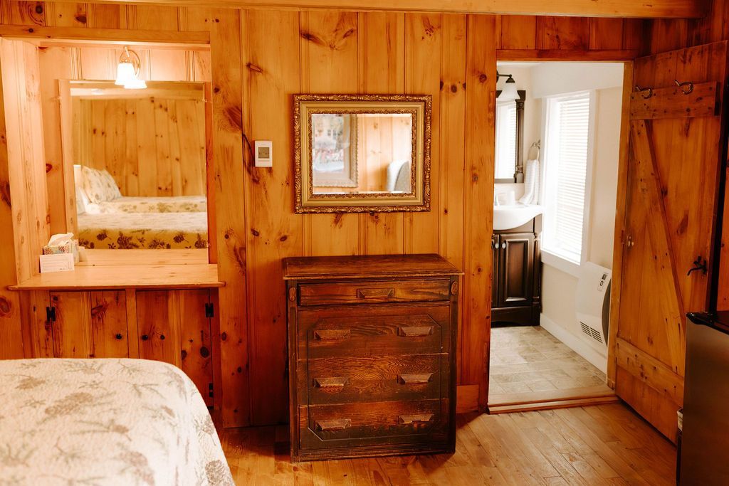 Wood-paneled bedroom with bed, dresser, mirror, and doorway to a bathroom