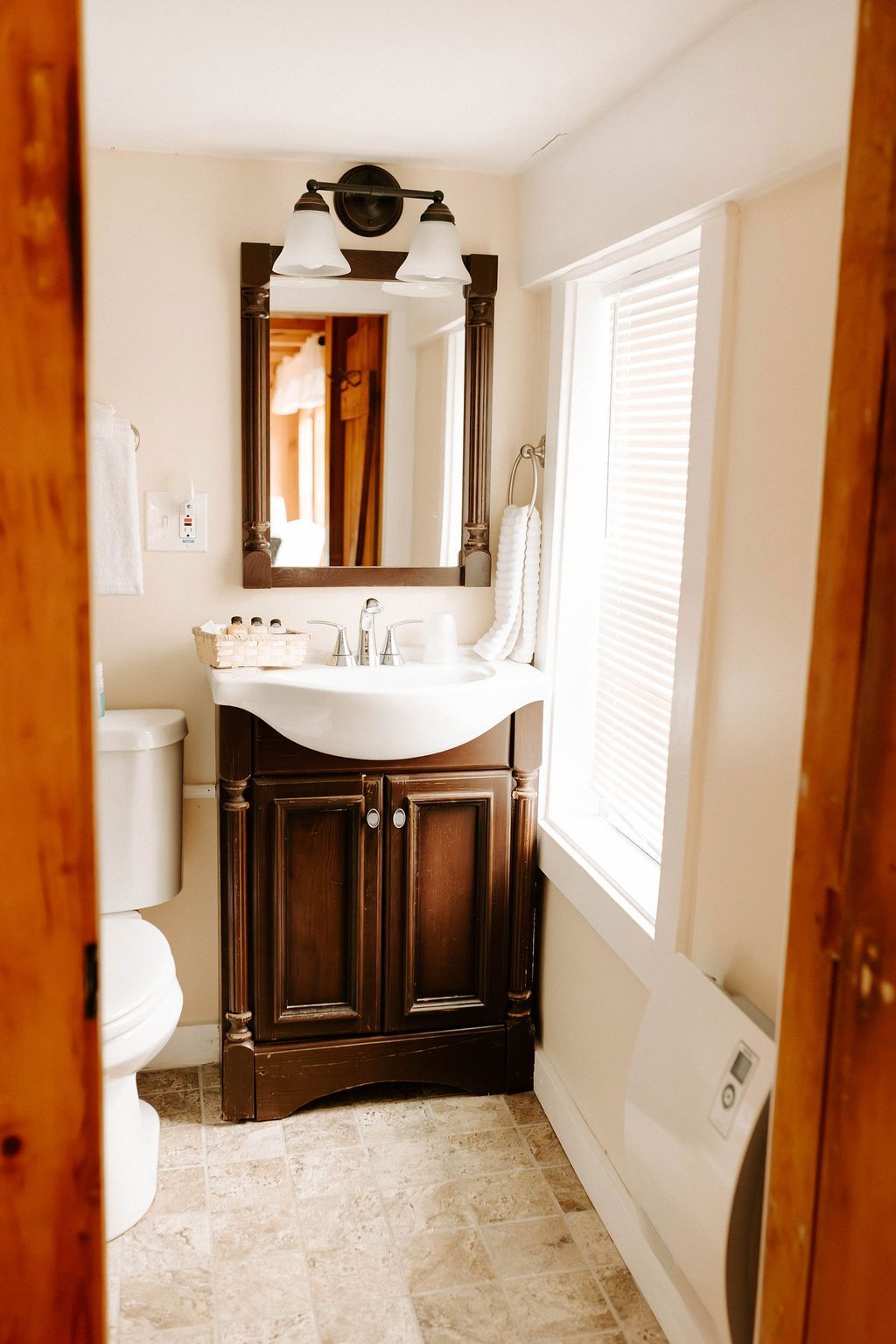 Narrow bathroom with dark wood vanity, white sink, mirror, and window blinds beside a bathtub