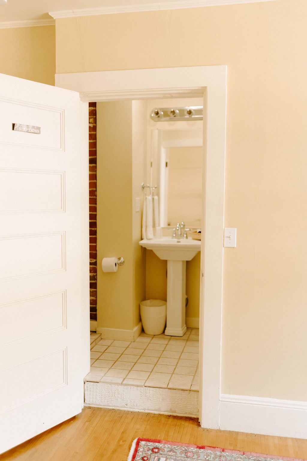 Open doorway to a small bathroom with beige walls, white sink, toilet, and tiled floor
