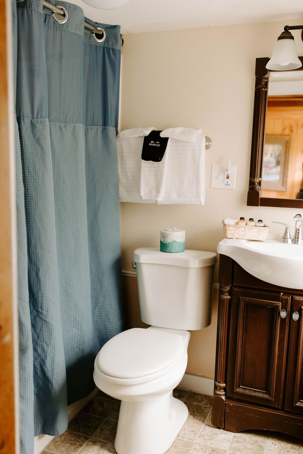 Bathroom with blue shower curtain, white toilet, sink vanity, and towels hanging on the wall.