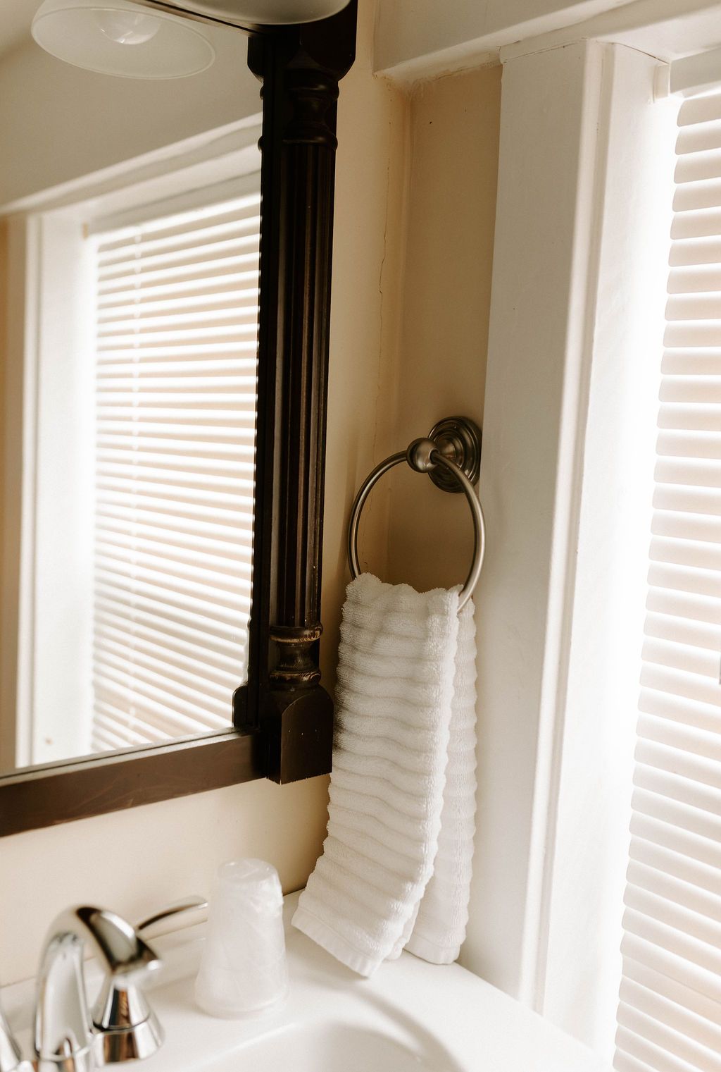 Bathroom vanity with mirror, chrome faucet, white soap dispenser, and towel ring holding folded white hand towels.