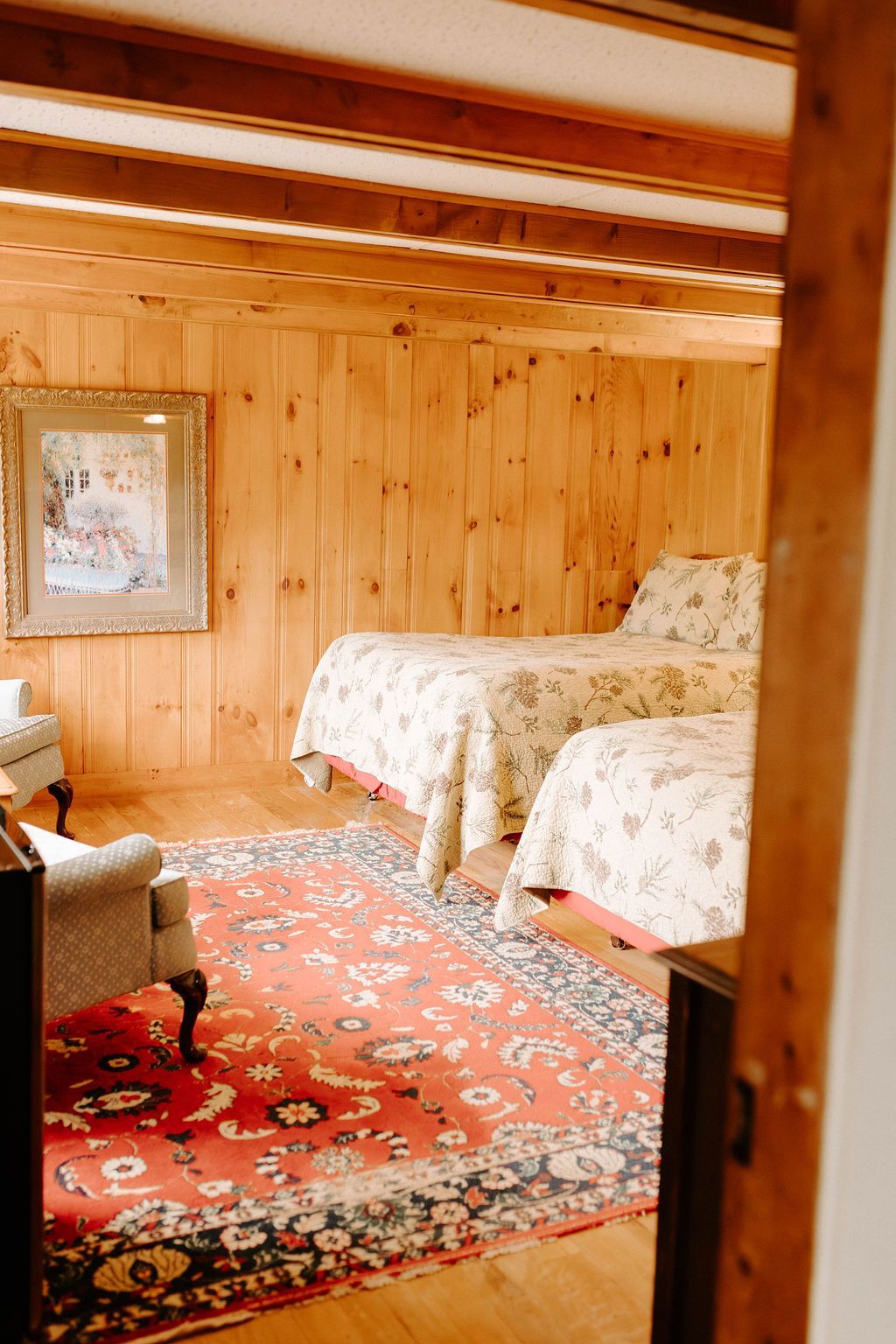 Wood-paneled bedroom with two twin beds and a red patterned rug