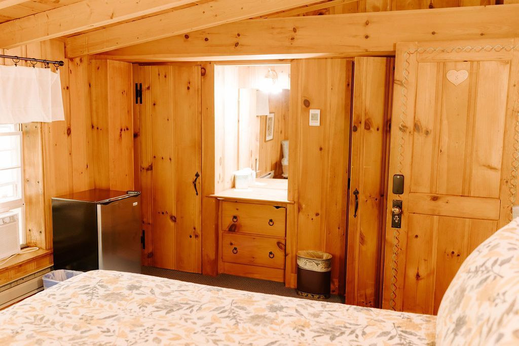 Wood-paneled bedroom with bed, mirror, and wooden doors under a sloped ceiling