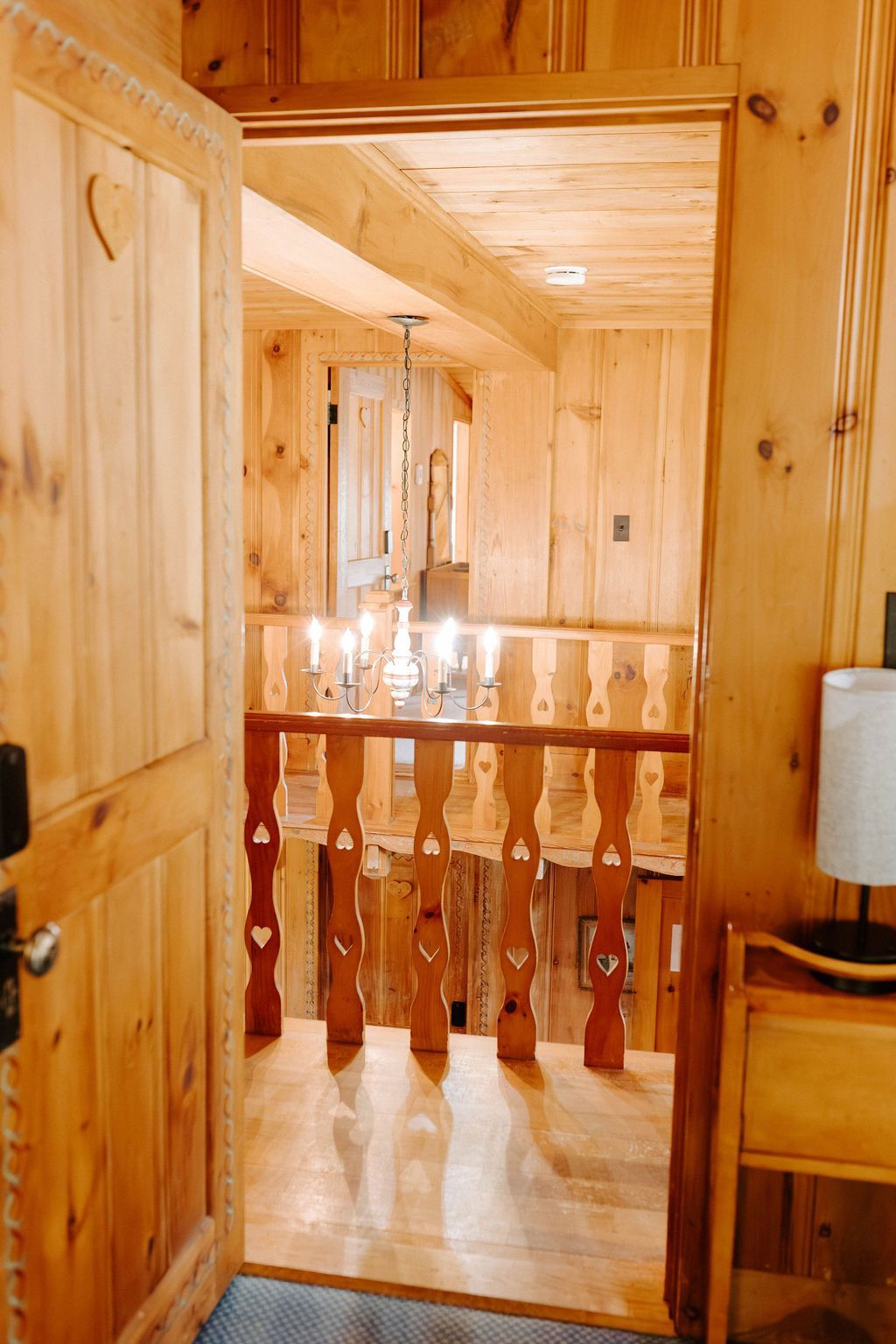 Wood-paneled interior hallway with a wooden stair railing and a small table lamp on the right