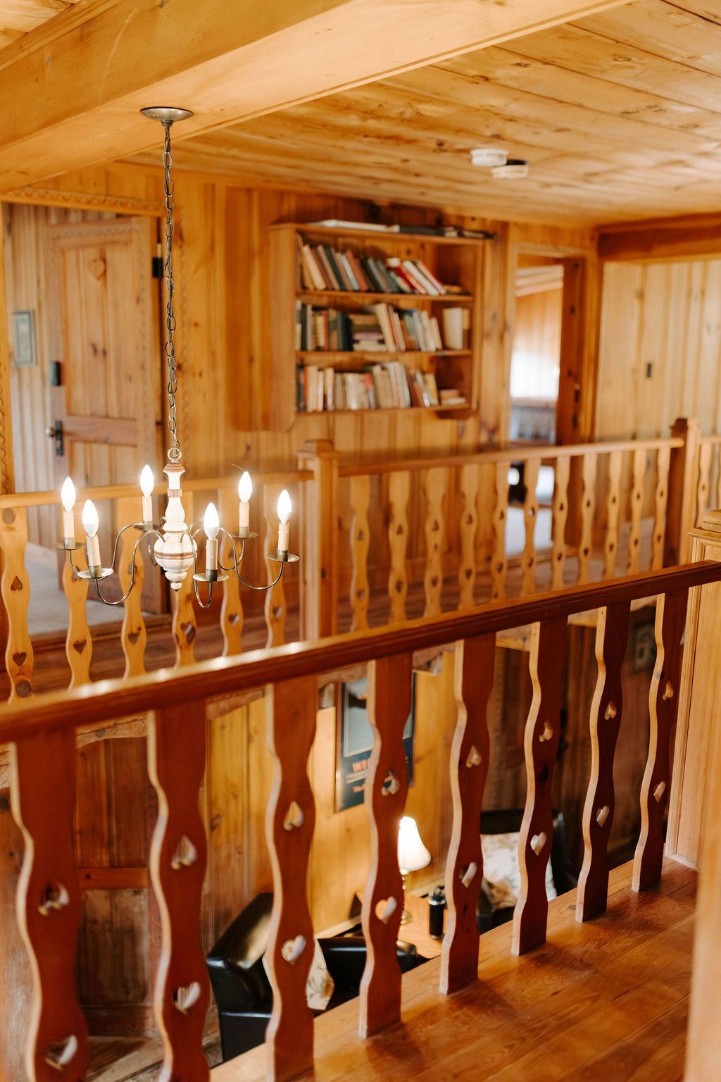 Wood-paneled loft with a bookshelf, railing, and chandelier in a cozy cabin interior