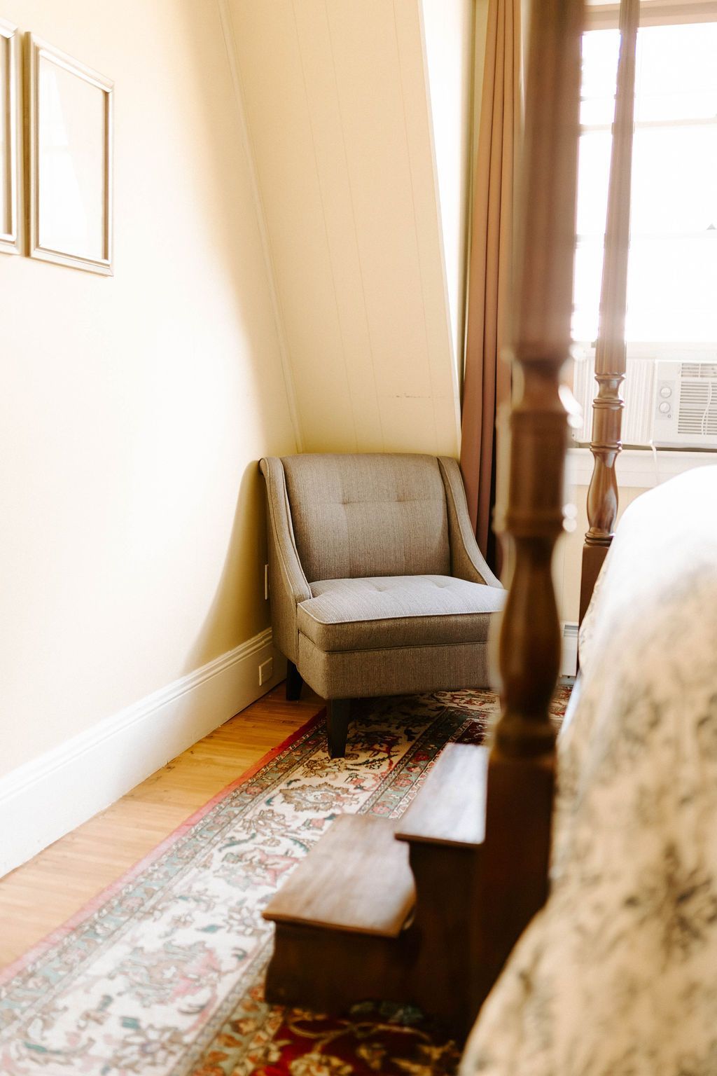 Small upholstered armchair by a sunlit window in a narrow, carpeted hallway