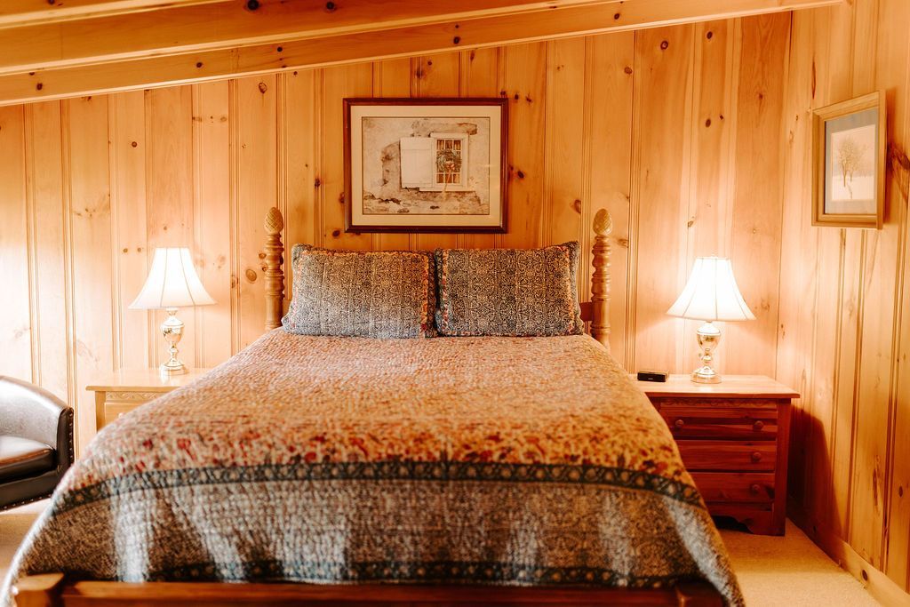 Wood-paneled bedroom with a large bed, two bedside lamps, and framed artwork above the headboard