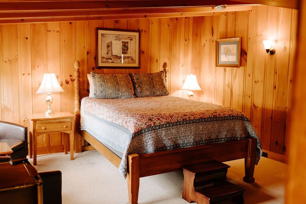 Cozy wood-paneled bedroom with a bed, bedside tables, lamps, and framed wall art.