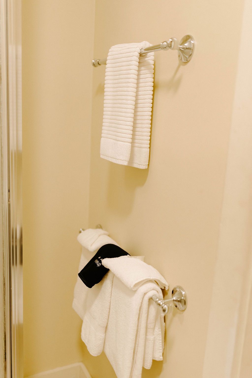 Two white towels hanging on chrome bathroom towel bars against a beige wall