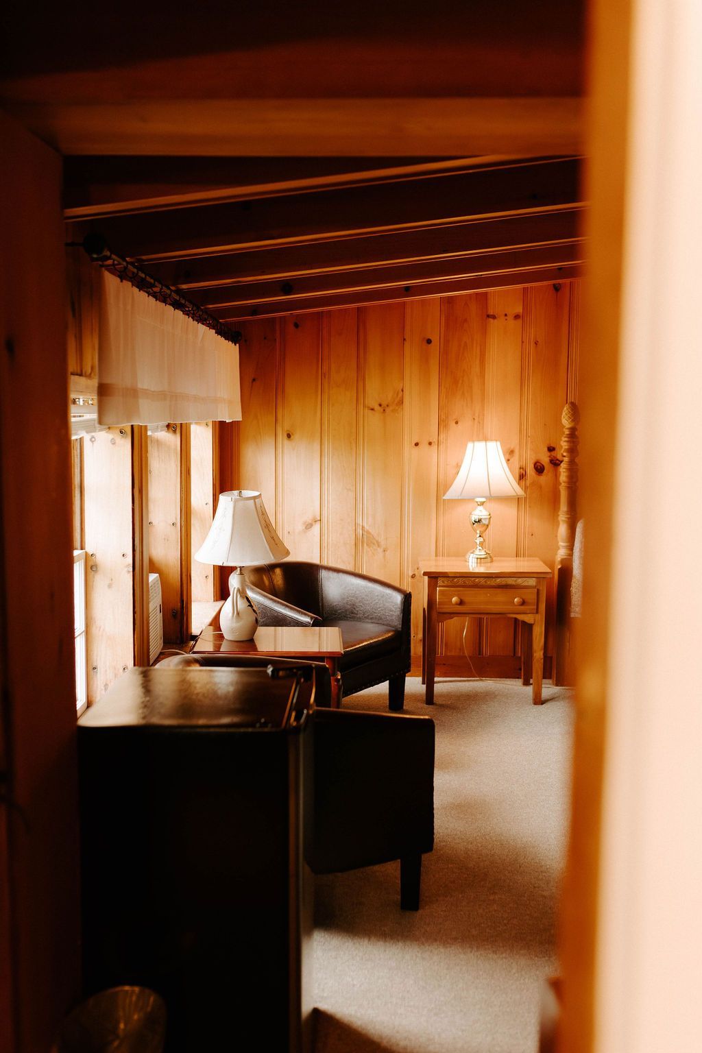 Cozy wooden cabin bedroom with a bed, desk, lamp, and warm amber lighting