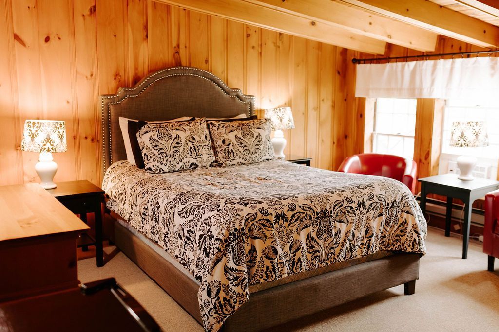 Cozy wood-paneled bedroom with a bed, bedside lamps, and a red chair by the window.