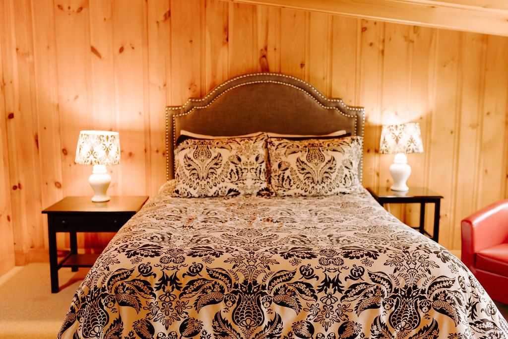 Cozy bedroom with a patterned bedspread, wood-paneled walls, and matching bedside lamps