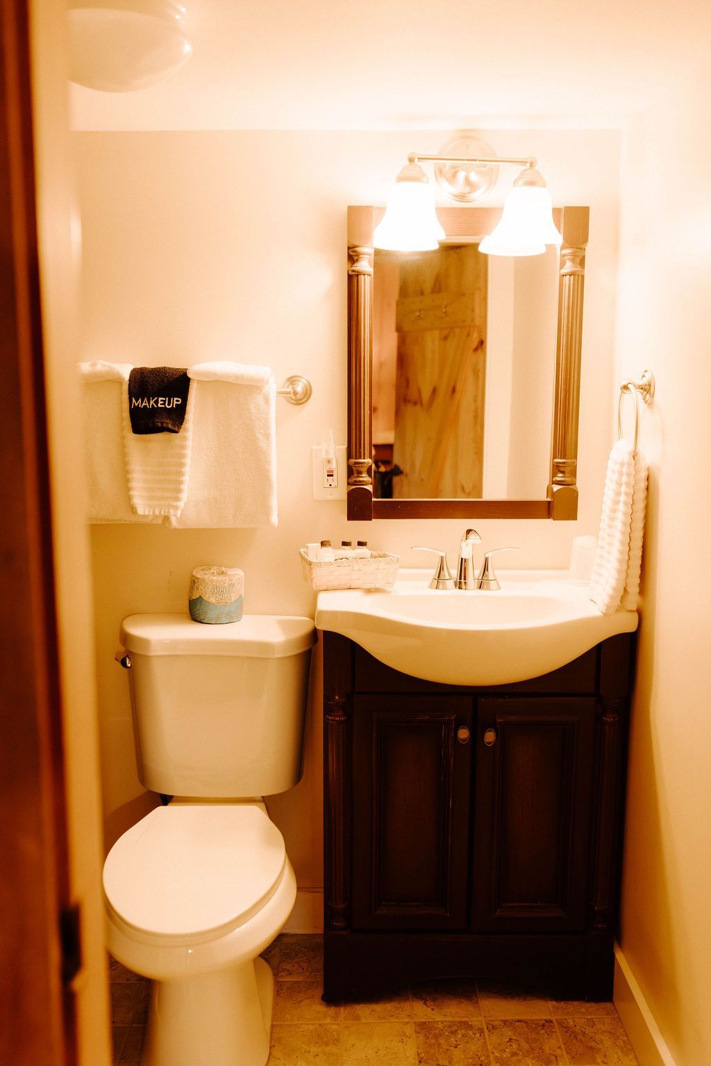 Small beige bathroom with toilet, pedestal sink, mirror, and dark wood vanity.