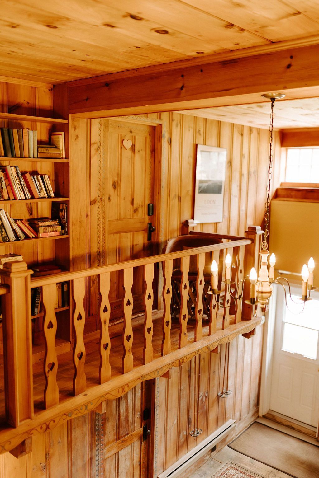 Wood-paneled loft hallway with a wooden railing, bookshelves, and a bright door below