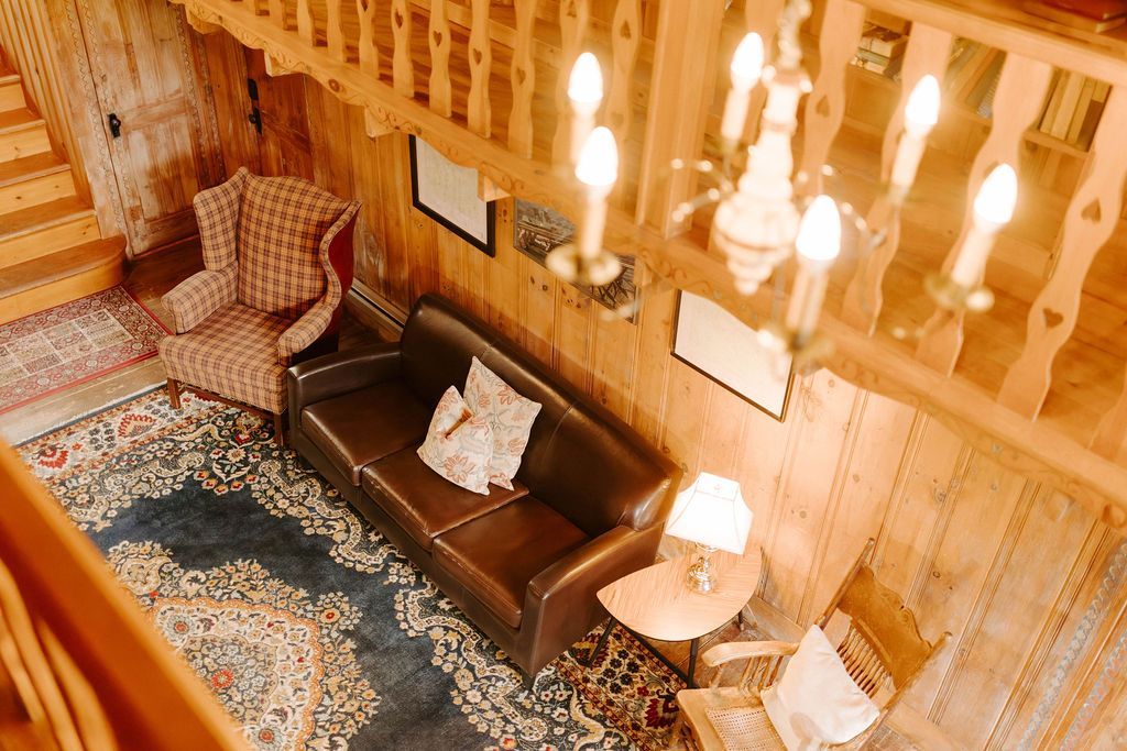 Cozy wood-paneled living room with brown sofa, patterned rug, armchair, and hanging lights