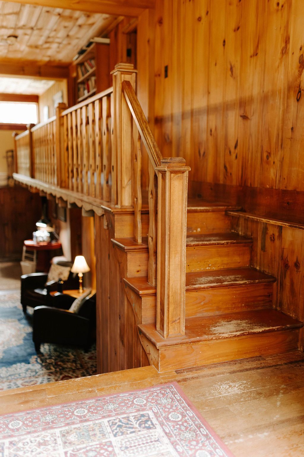 Wooden staircase with polished banister in a rustic wood-paneled interior hallway