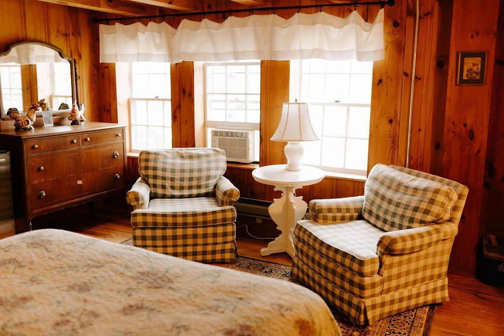 Cozy rustic cabin bedroom with plaid armchairs, wood-paneled walls, and a bed by a window