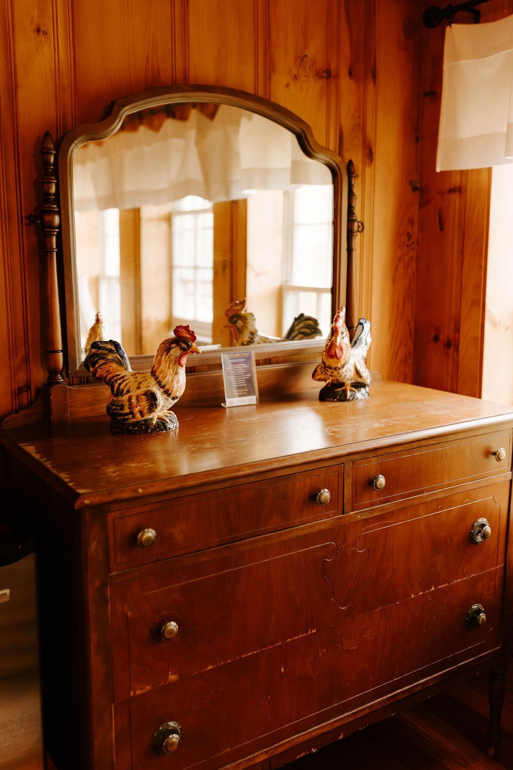 Wooden dresser with an ornate mirror in a cozy sunlit room, decorated with small figurines on top