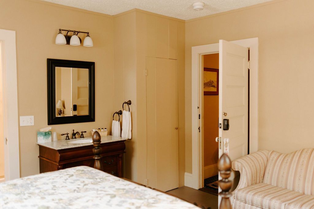 Beige bedroom with dresser, mirror, open door, and striped couch.