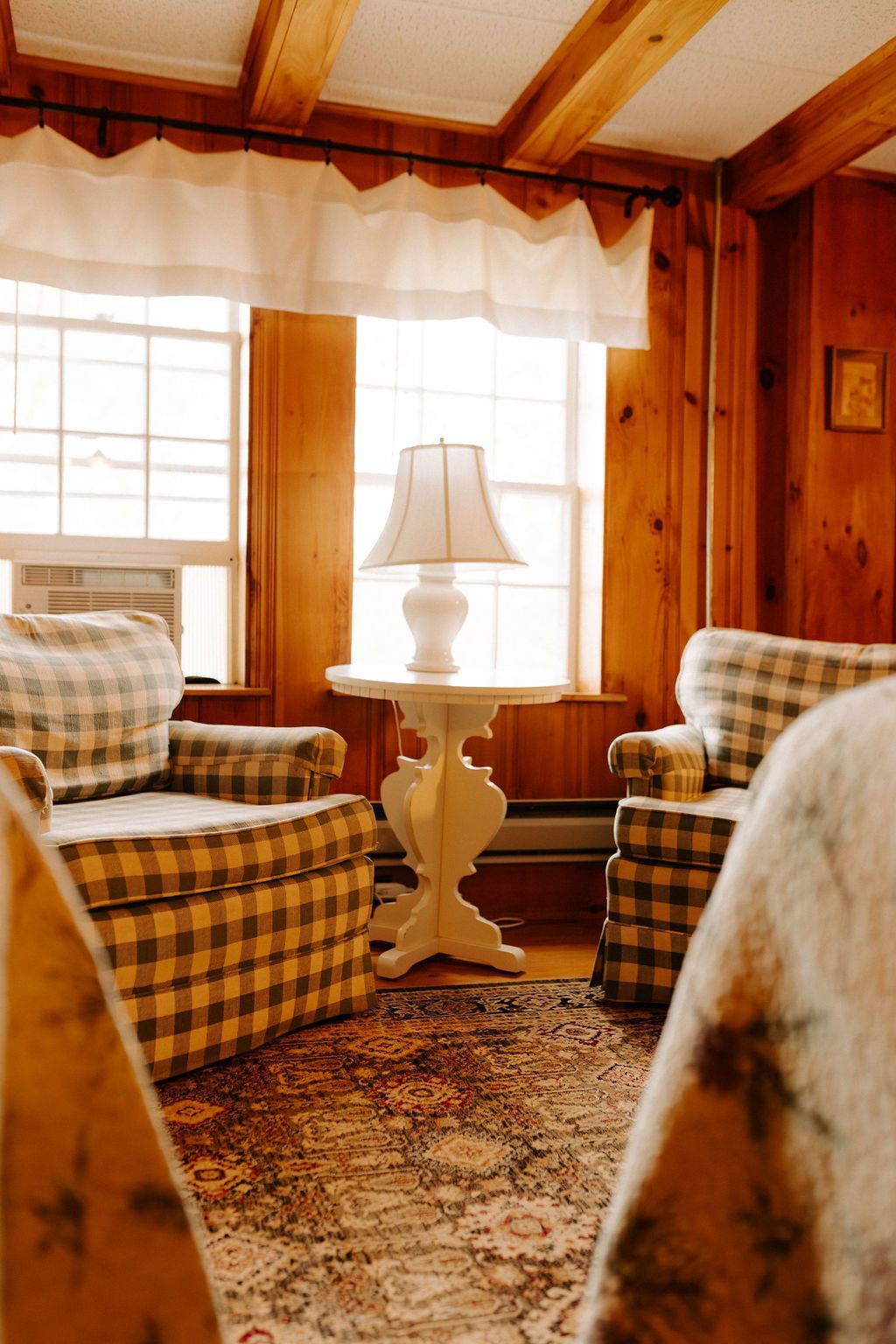 Cozy wood-paneled room with plaid chairs, a white lamp, and a large window