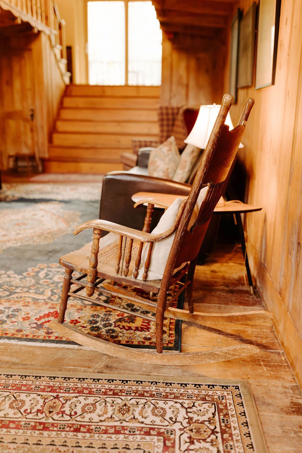 Wooden rocking chair in a rustic hallway with patterned rugs and stairs in the background