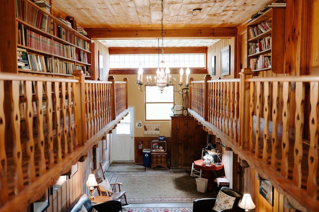 Cozy loft library with wooden bookshelves, railings, and a bright window at the far end.