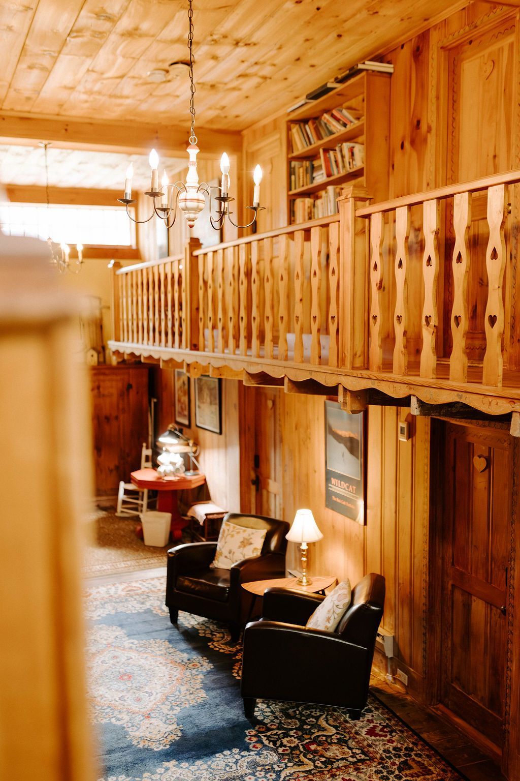 Cozy wood-paneled cabin interior with loft railing, blue rug, and black armchairs by a lamp