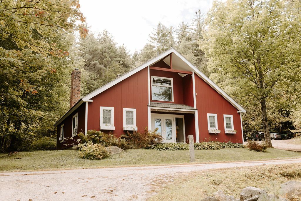 Red house with white trim surrounded by trees on a rural property.