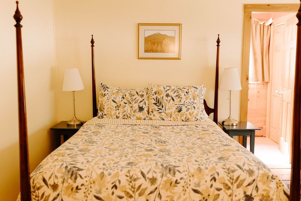 Bedroom with a bedspread, four-poster bed, nightstands, lamp, and open doorway to a bathroom