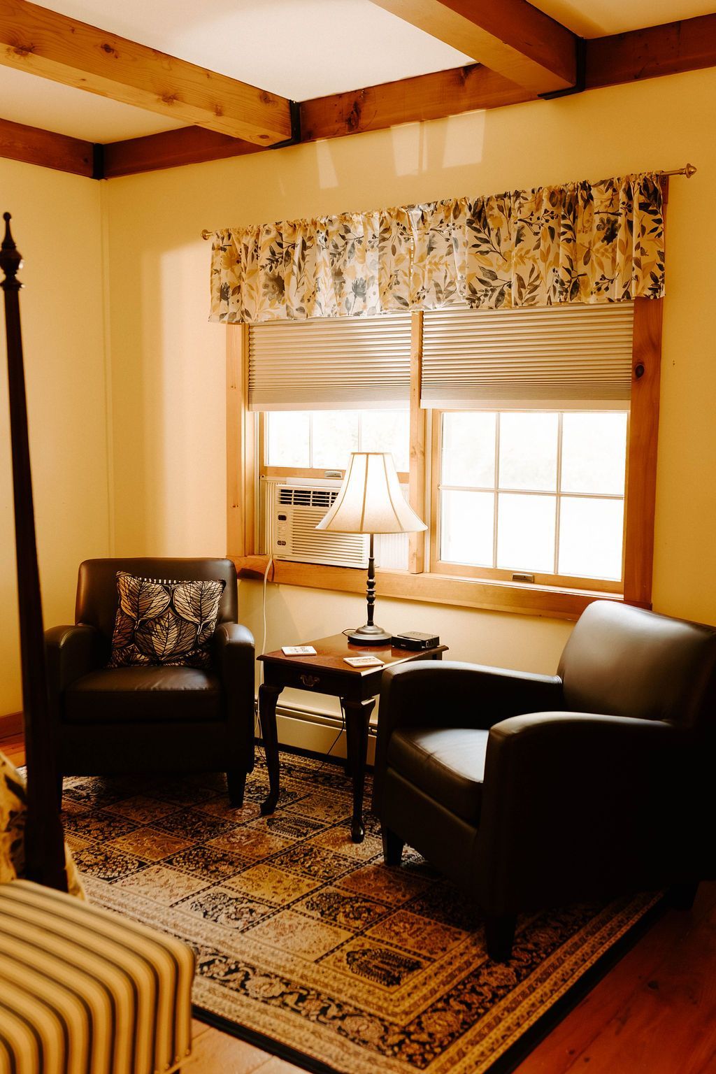 Cozy living room with wooden beams, window seat, lamp, armchairs, and patterned rug