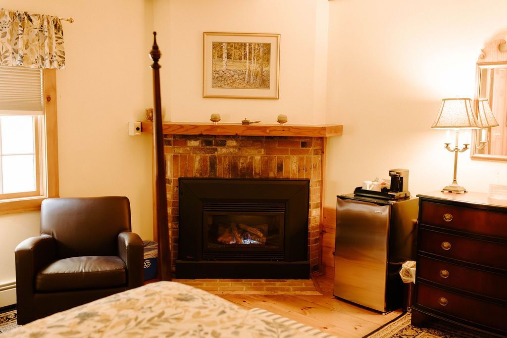 Cozy living room with a fireplace, armchair, lamp, framed art, and wooden dresser.